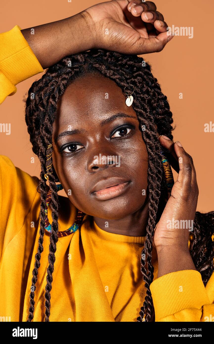 Stock photo of confident black woman with braids posing in studio shot against brown background. Stock Photo