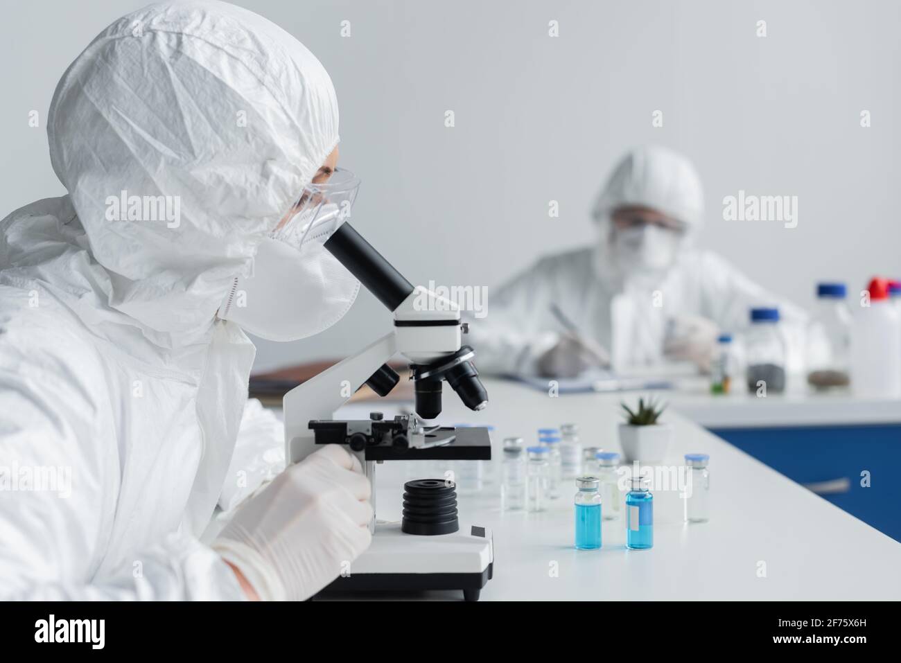 Scientist using microscope near jars with vaccines Stock Photo