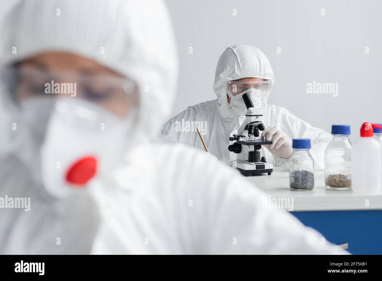Scientist using microscope while working near colleague on blurred foreground Stock Photo