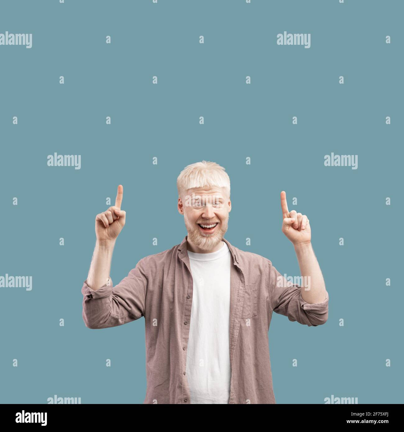 Special offer. Joyful young albino guy pointing fingers up on copy space text or product on color background Stock Photo