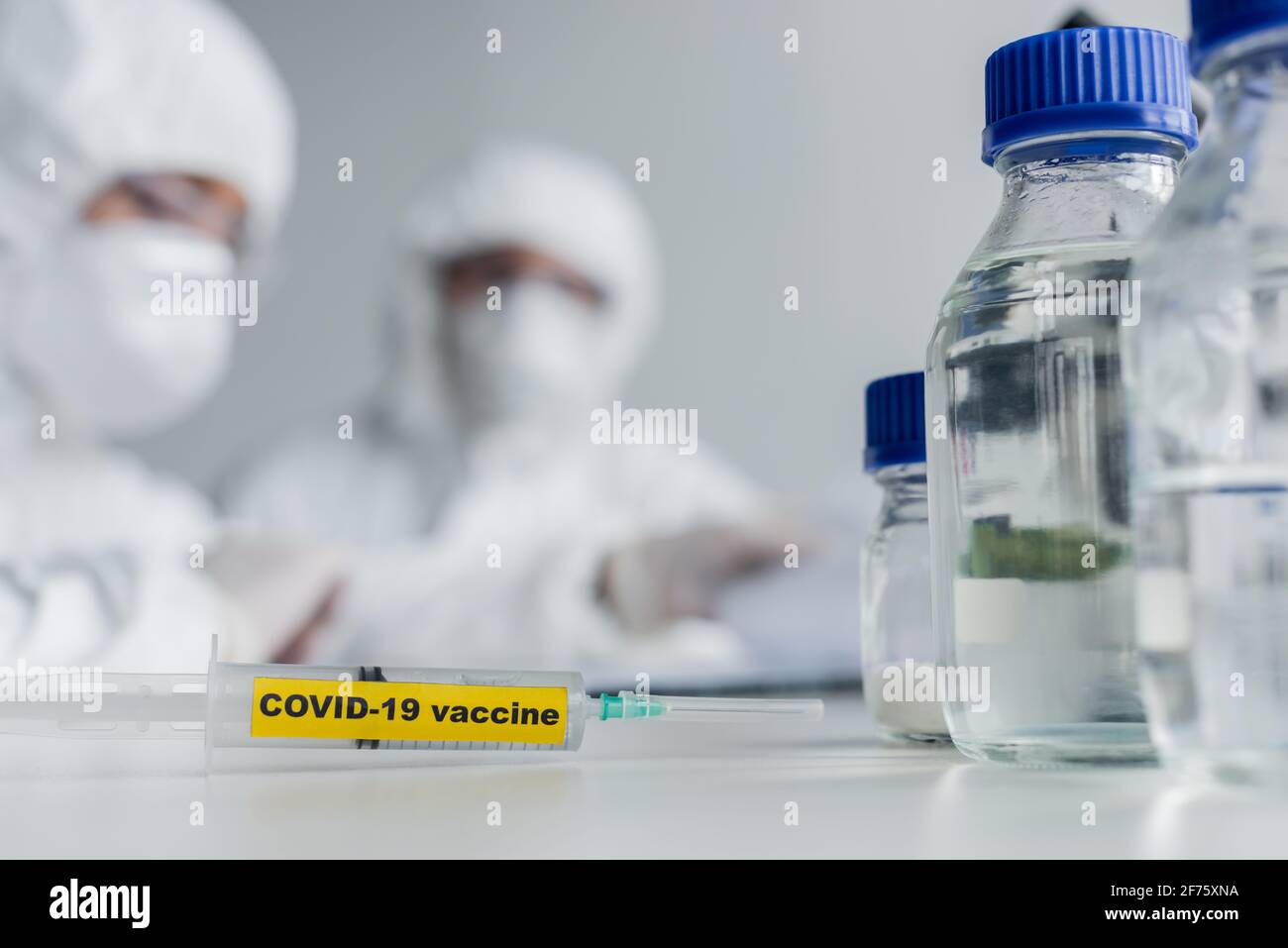 Syringe with covid-19 vaccine lettering near scientists in laboratory Stock Photo