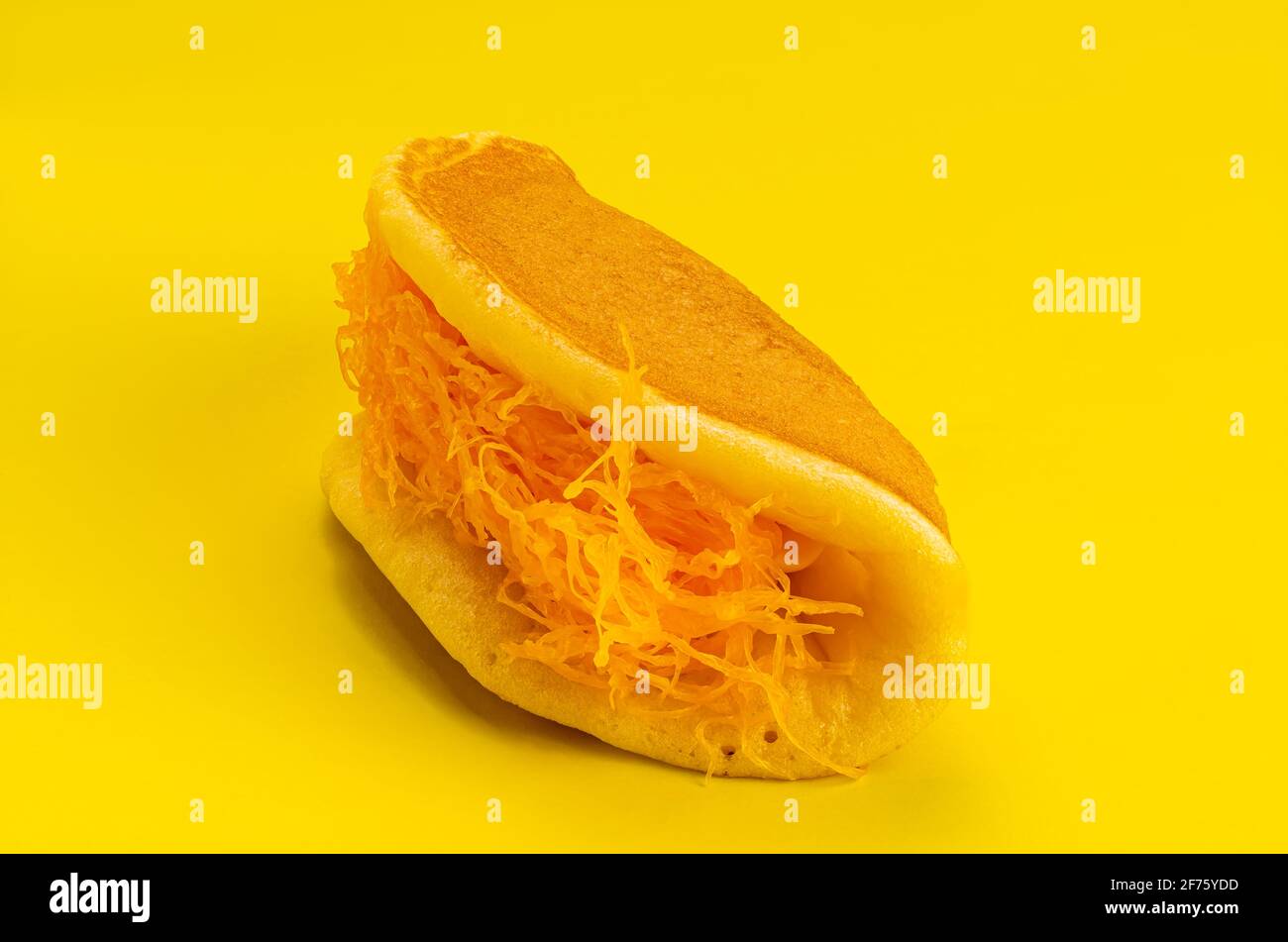 Side view of closeup homemade thick pancake filling with egg yolk threads on yellow background. View of homemade dessert pancake. Stock Photo