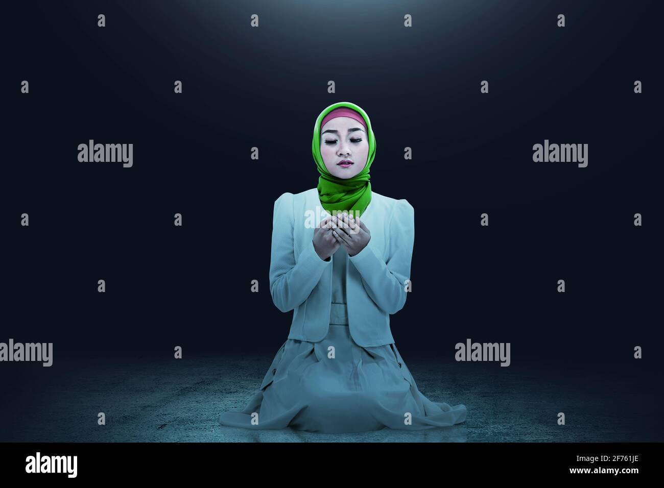 Asian Muslim woman in a veil sitting while raised hands and praying ...