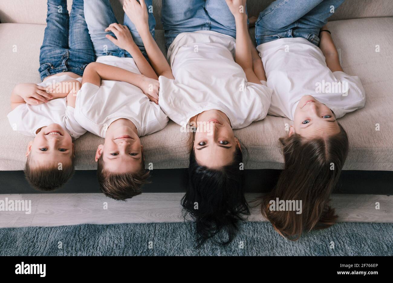 My mom, my best friend Beautiful smiling brunette mother and children lower their heads from the sofa and look at the camera. Stock Photo