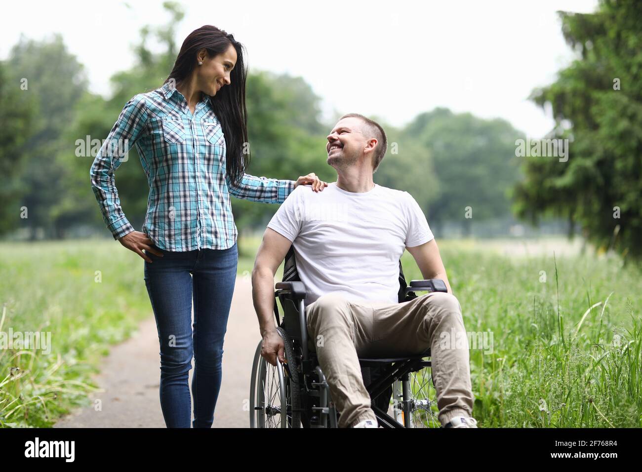 Smiling man in wheelchair walks in park with woman Stock Photo - Alamy