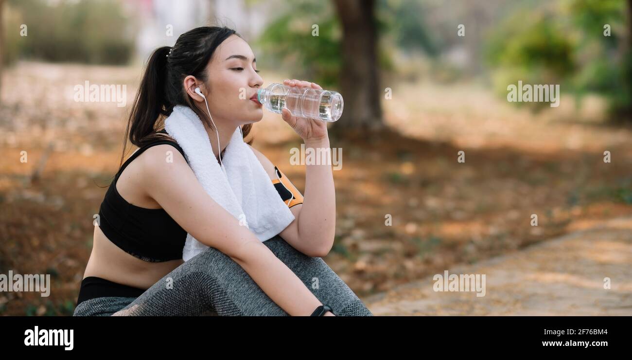 Young woman athlete takes a break, drinking water, out on a run on a hot day. Stock Photo