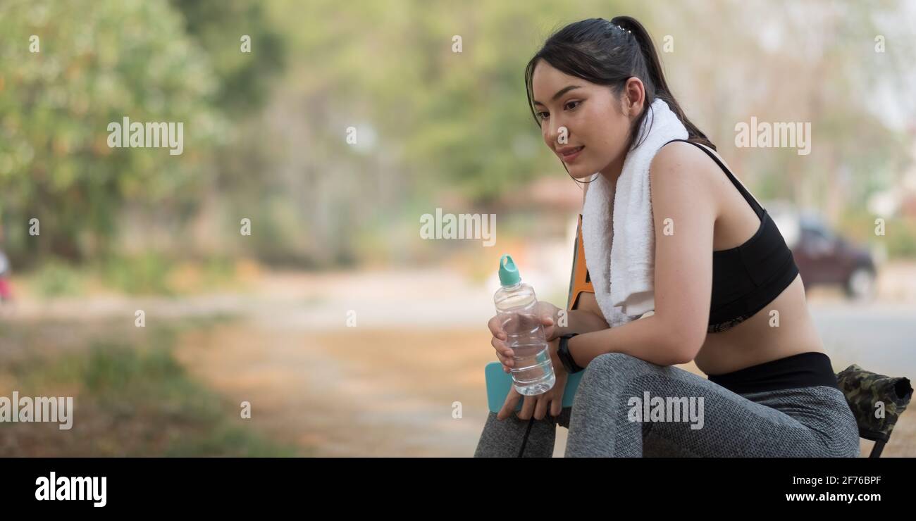 Young athletic woman holding water from a bottle after running in the park Stock Photo