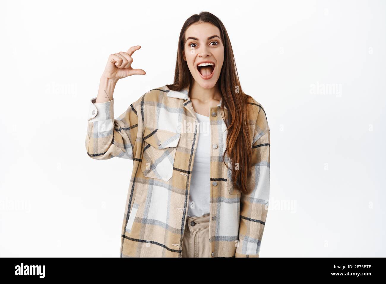 Excited young woman holding something little and awesome, scream from joy and amazement as hold small size object on copyspace, standing over white Stock Photo