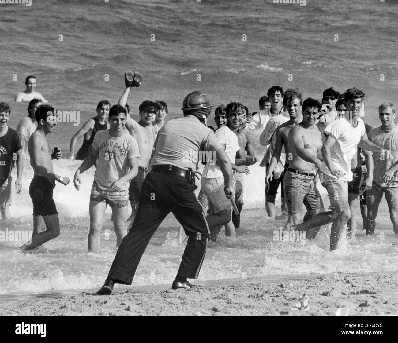 Students riot during Spring Break at Ft. Lauderdale Beach.  Ca. 1960's.. Here taunting a police officer as he chases them into the surf. Stock Photo