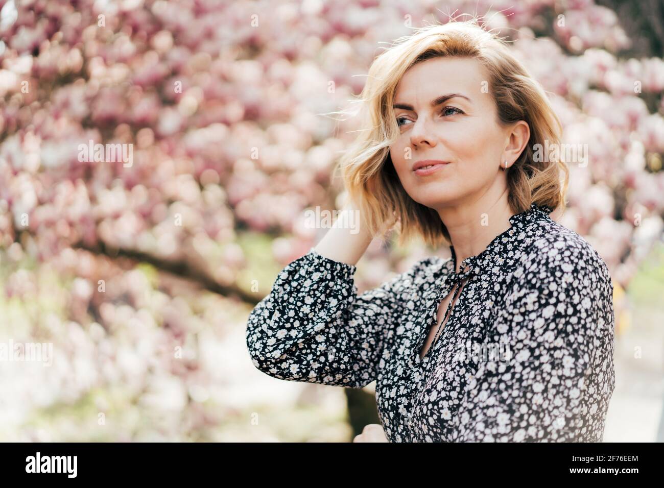 Portrait of a beautiful woman in her forties. Profile portrait with a pink flowering magnolia tree as background. Confident excellent graceful woman. Stock Photo