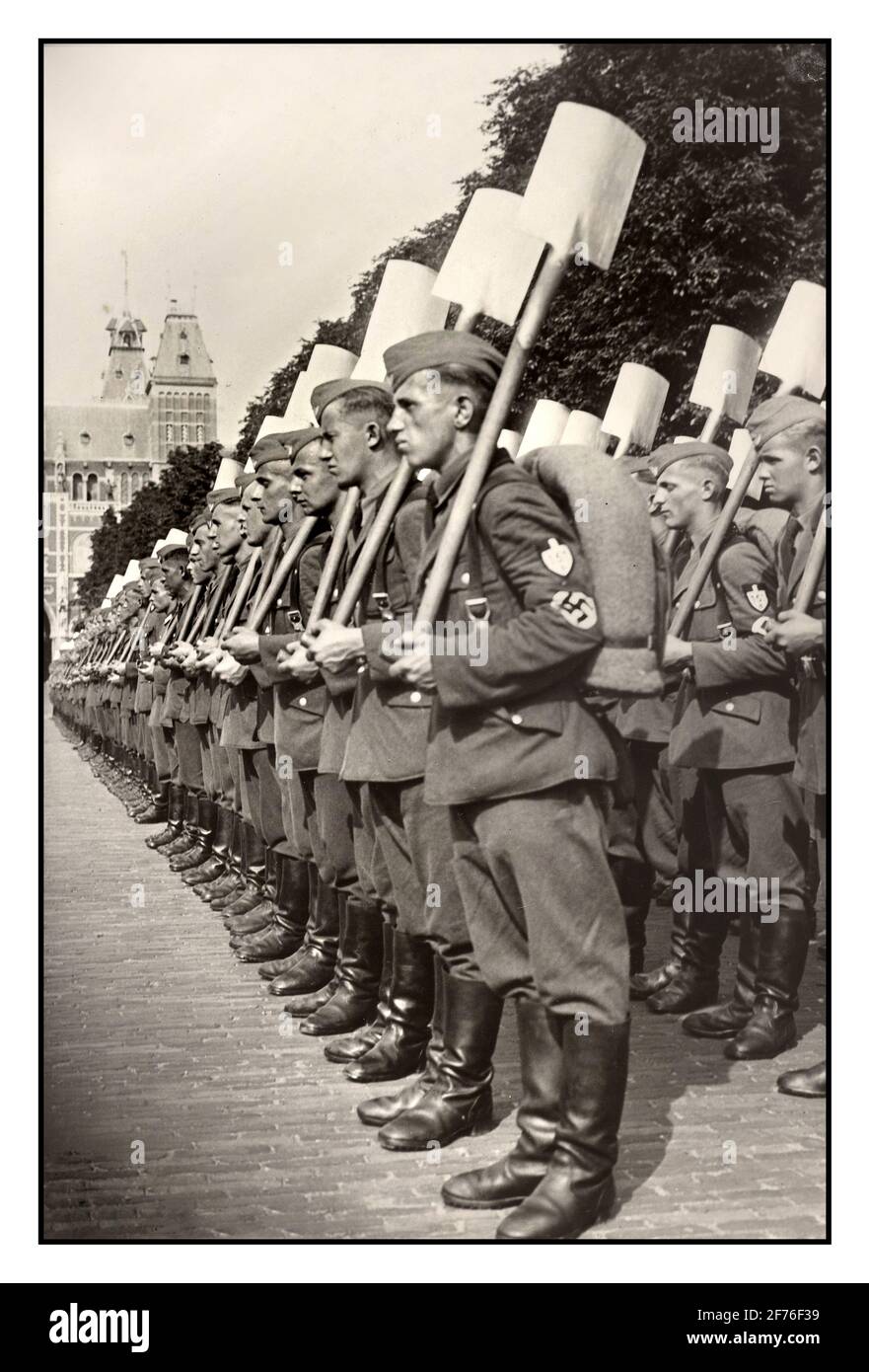 Nazi Germany RAD Parade Reich Labor Work Service Uniform Parade with shovels at attention. Archive 1940s WW2 In front of the Rijksmuseum; the German Reich Labor Service is set up for a parade for Seyss Inquart.; Aug 4; 1940 Amsterdam Holland The Reich Labour Service (Reichsarbeitsdienst; RAD) was a major organisation established in Nazi Germany as an agency to help mitigate the effects of unemployment on the German economy, militarise the workforce and indoctrinate with Nazi ideology. It was the official state labour service, divided into separate sections for men and women. World War II Stock Photo