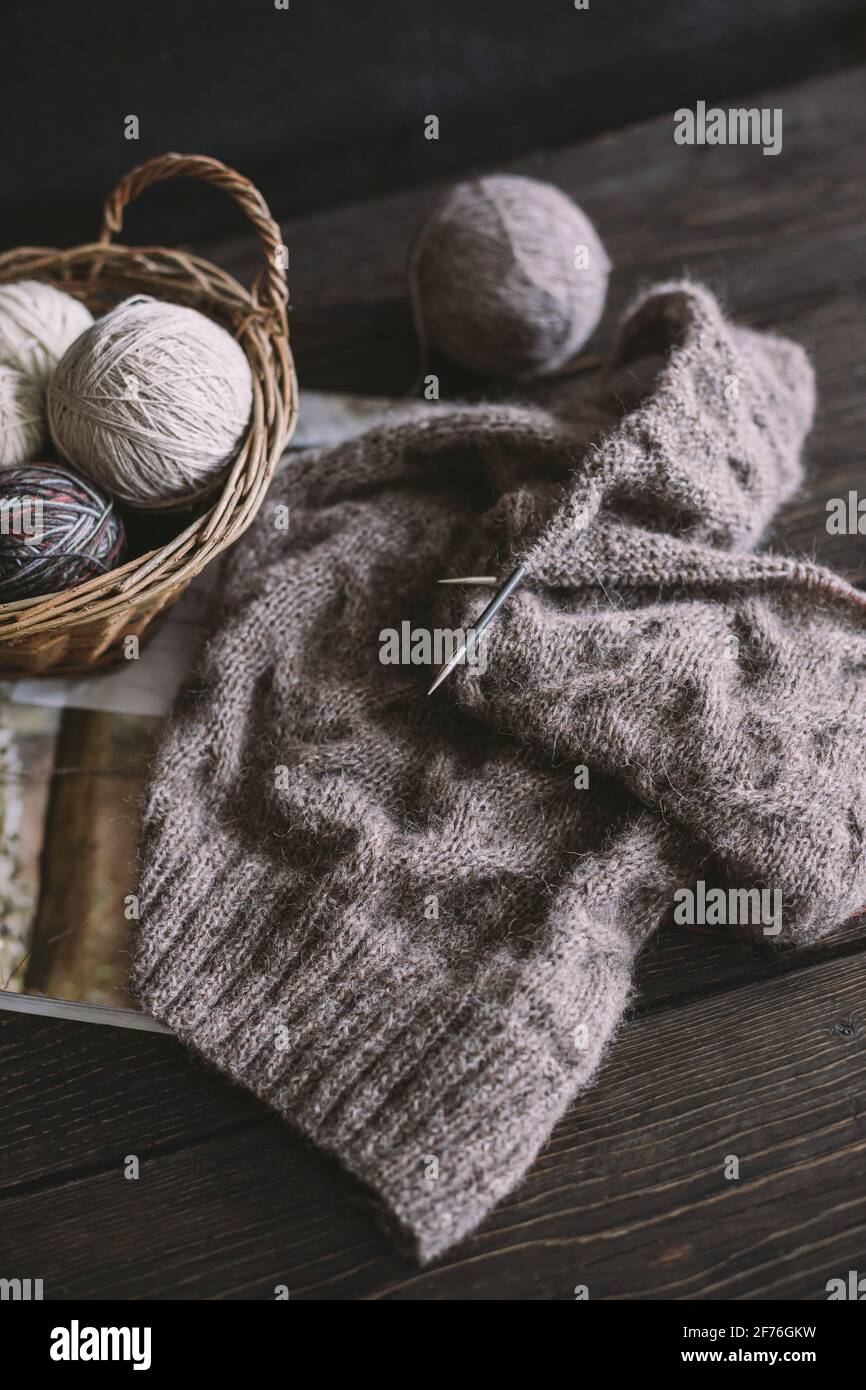 Hand knitting with needles and yarn balls in a basket on a dark ...