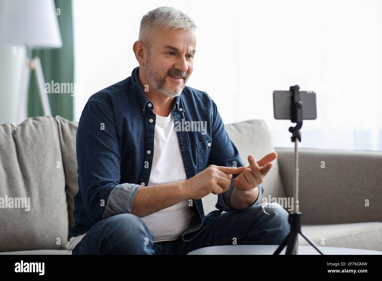 Cheerful matured man broadcasting from home, using smartphone Stock Photo