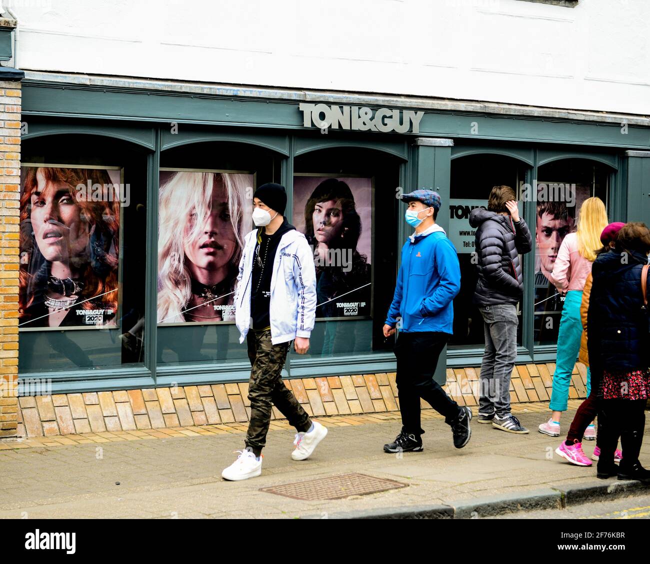 Cambridge, UK, England, 03-04-2021. Adults wearing face coverings  walk pastBuilding exterior of Toni and Guy Hair Stylists. Stock Photo