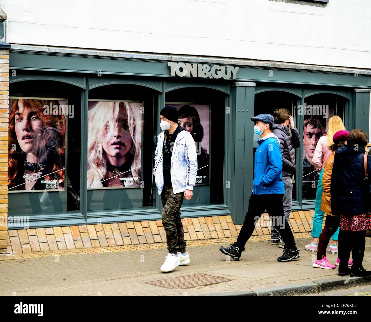 Cambridge, UK, England, 03-04-2021. Adults wearing face coverings  walk pastBuilding exterior of Toni and Guy Hair Stylists. Stock Photo