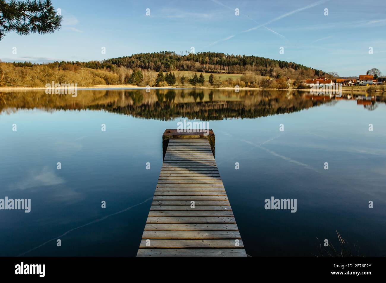 Empty wooden pier on lake. Spring pond village in background. Sunny calm idyllic weather. Serenity scenery.Meditation without people.Motivation quote. Stock Photo