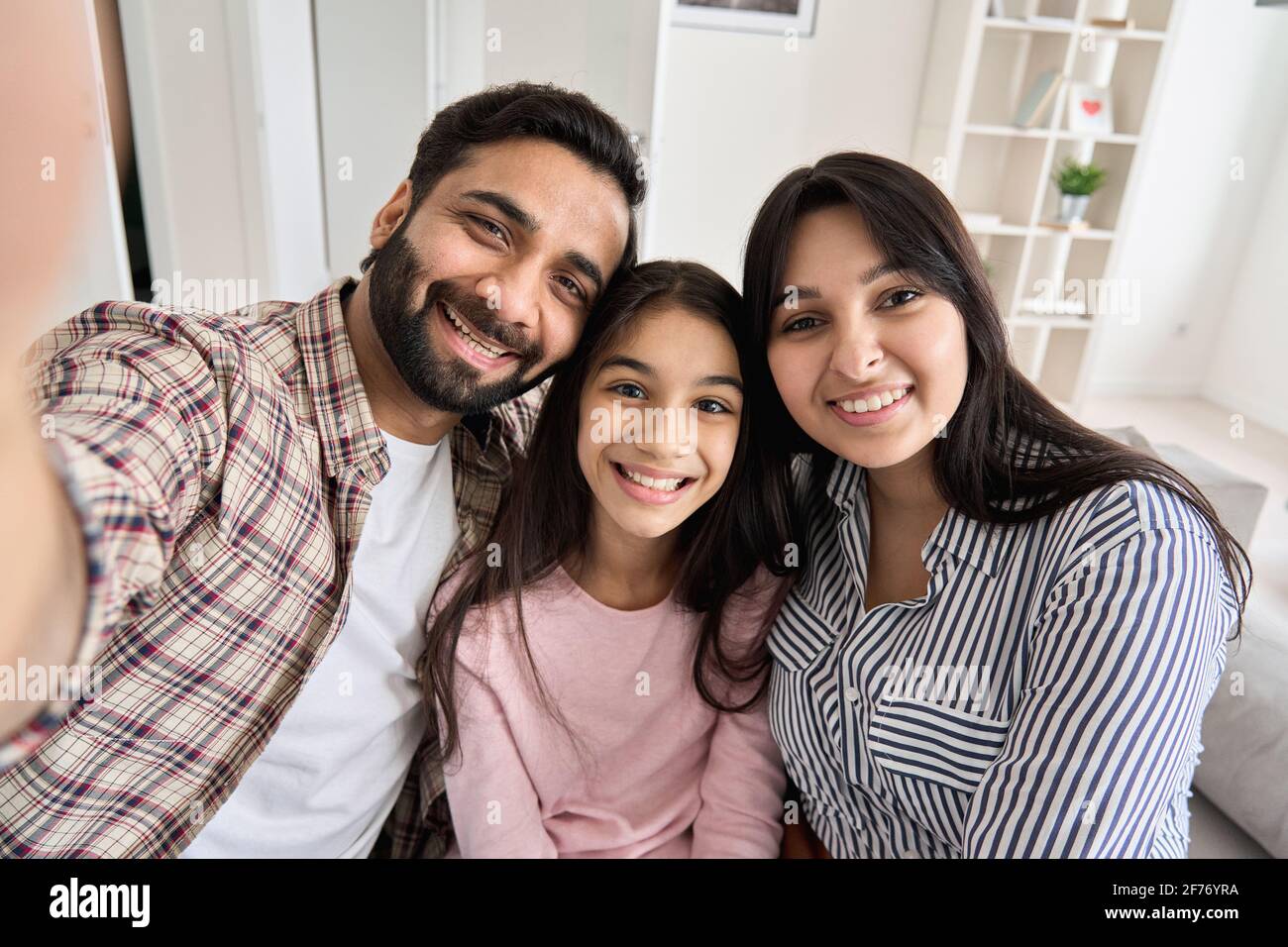 Happy indian couple and teen daughter taking selfie looking at phone camera. Stock Photo