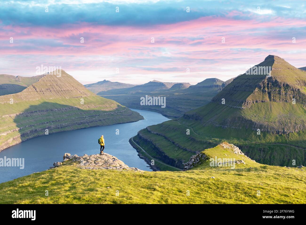 Lonely tourist in yellow jacket looking over majestic fjords of Funningur, Eysturoy island, Faroe Islands. Landscape photography Stock Photo