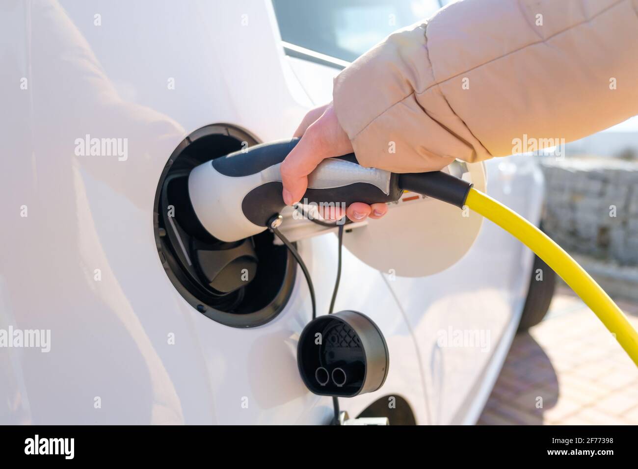 Close up woman hand inserts power cable supply to charge electric or EV car. Stock Photo