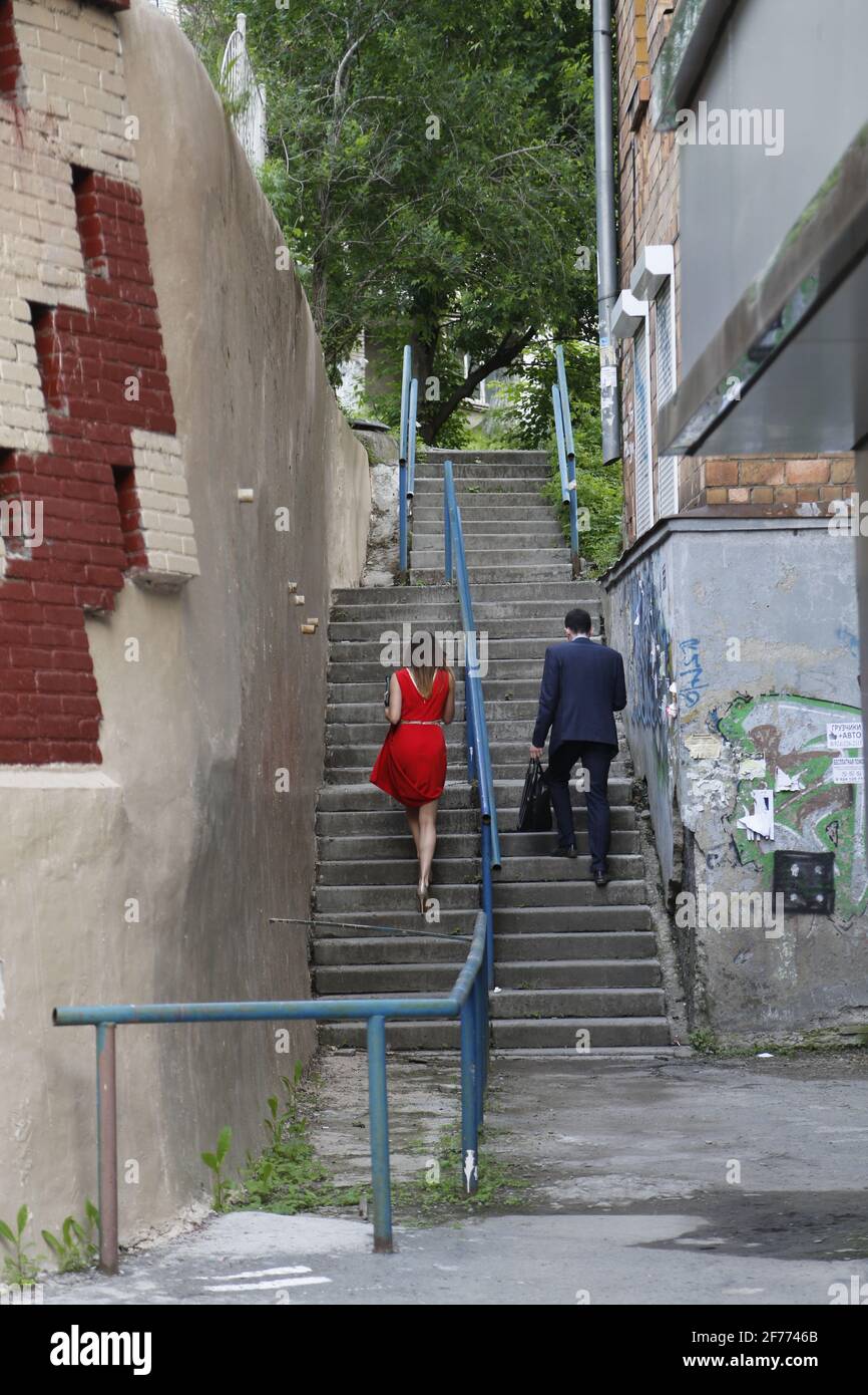 Female in red dress and man in costume climb stairs next to each other, in parallel, separated by a railing. Concept of gender inequality career path Stock Photo