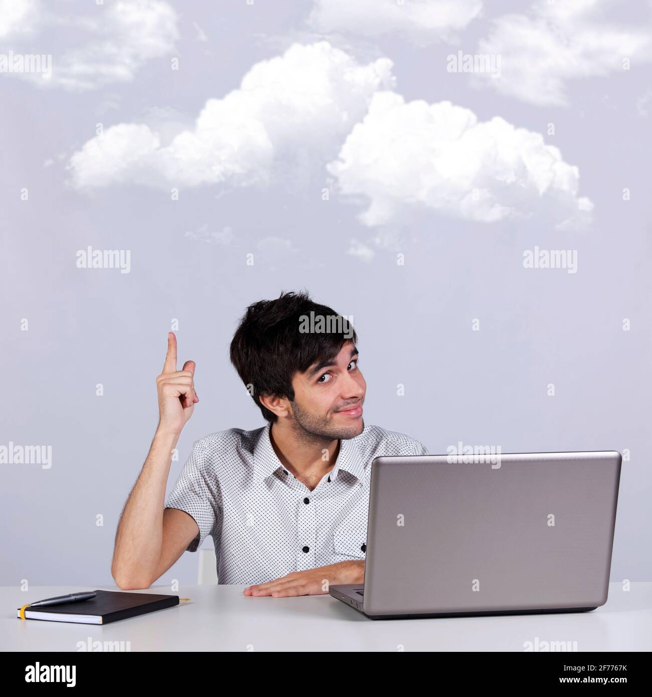 Young man working with his laptop  pointing to the cloud (cloud computing concept) Stock Photo