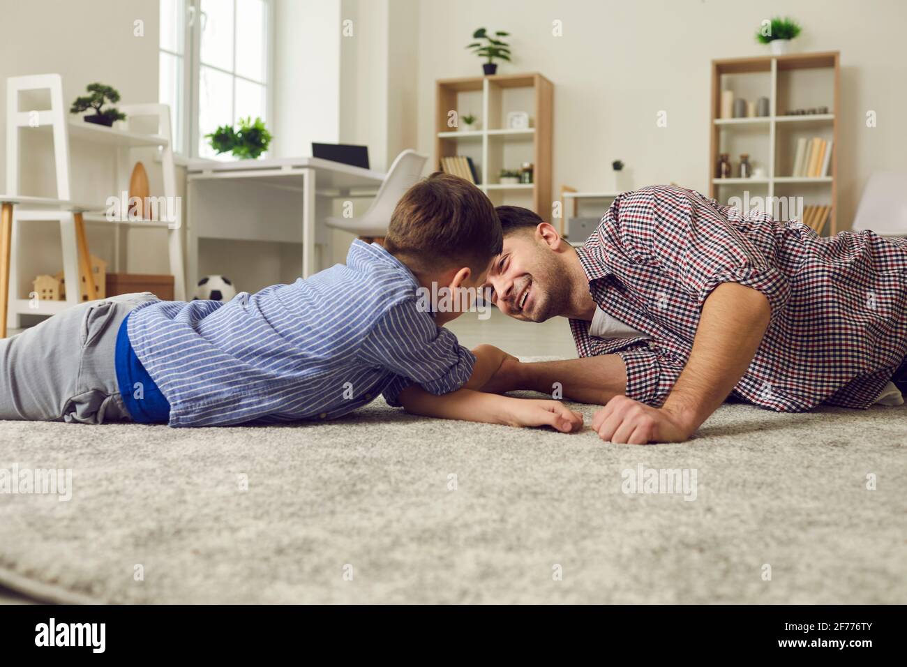 Side view of happy father and son competing in arm wrestling lying on the floor at home. Stock Photo