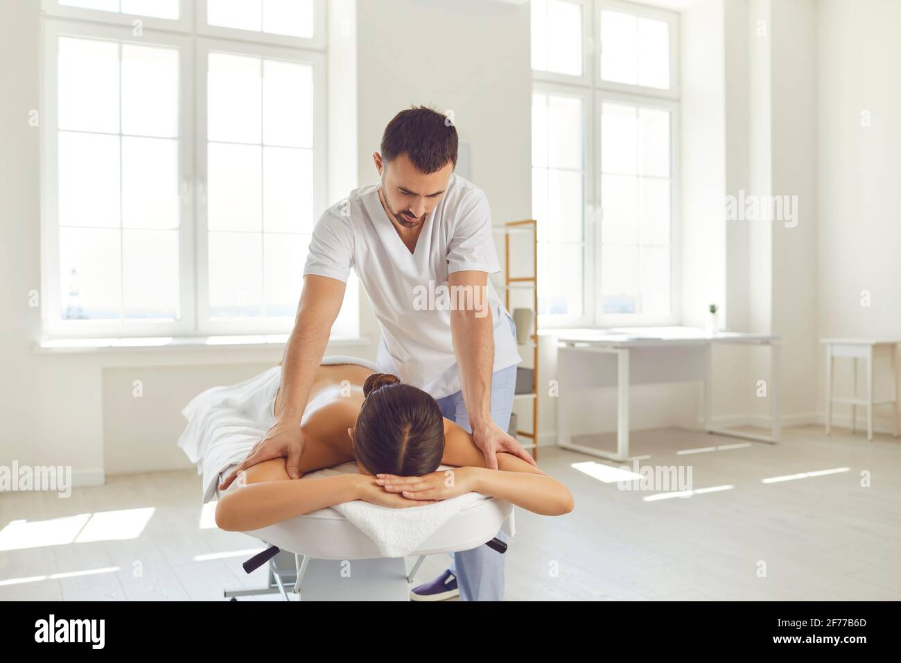 Masseur or manual therapist doing relaxing body massage for young woman lying on massage table Stock Photo