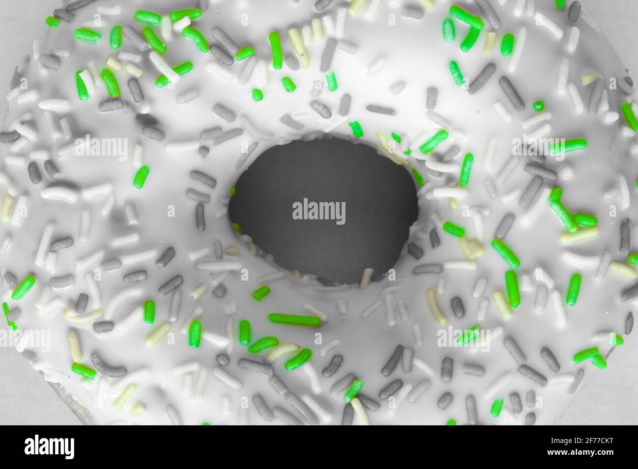 Flat-lay image of ring donut with white glaze and hundreds and thousands, black and white image with selected green colour Stock Photo