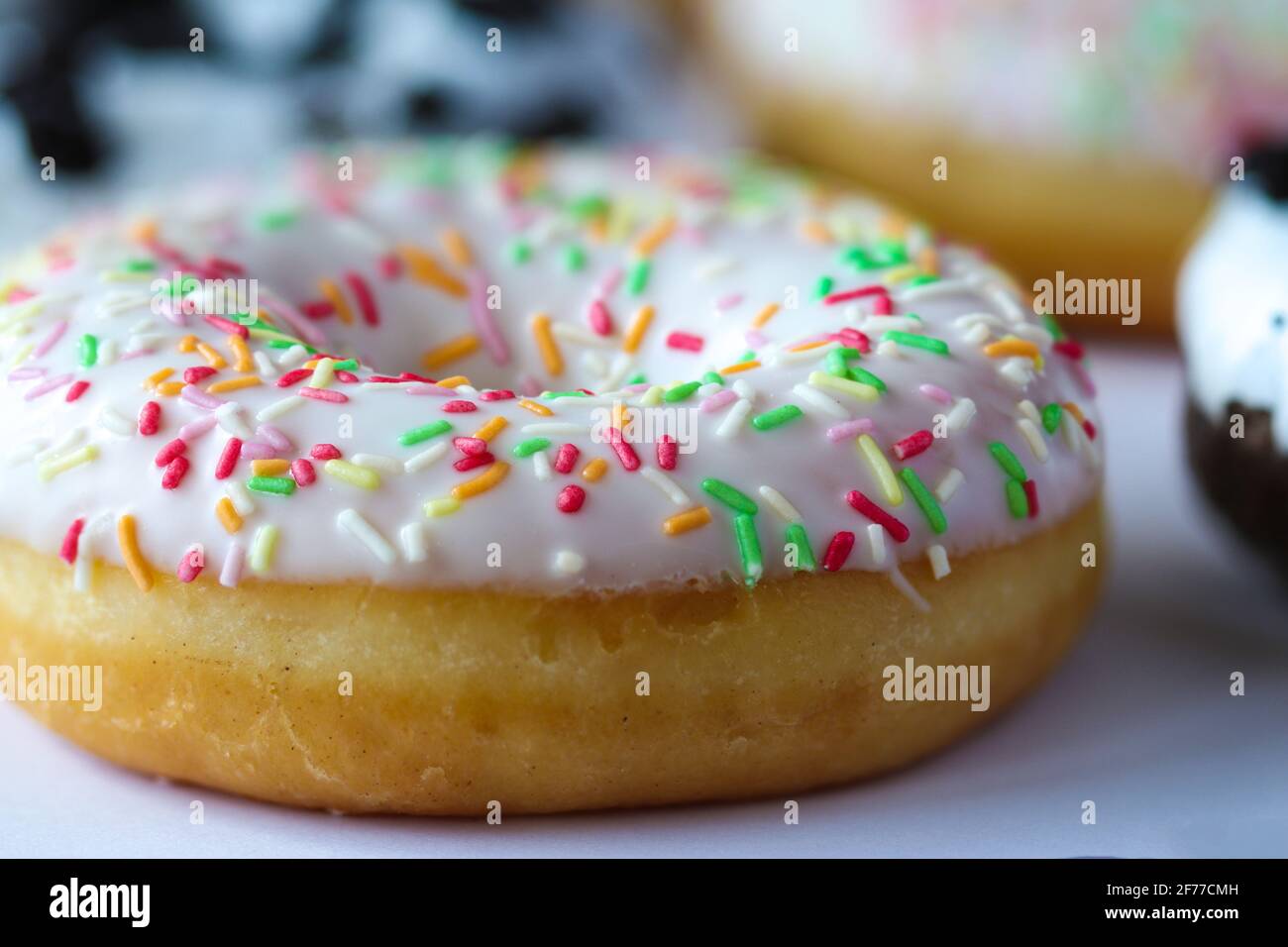 Close-up on ring donut with white glaze and colourful hundreds and thousands Stock Photo