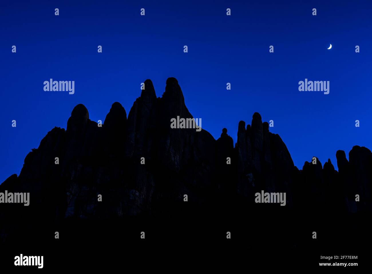 Crescent moon behind the silhouette of Montserrat spires at blue hour (Barcelona province, Catalonia, Spain) ESP: Luna creciente detrás de Montserrat Stock Photo