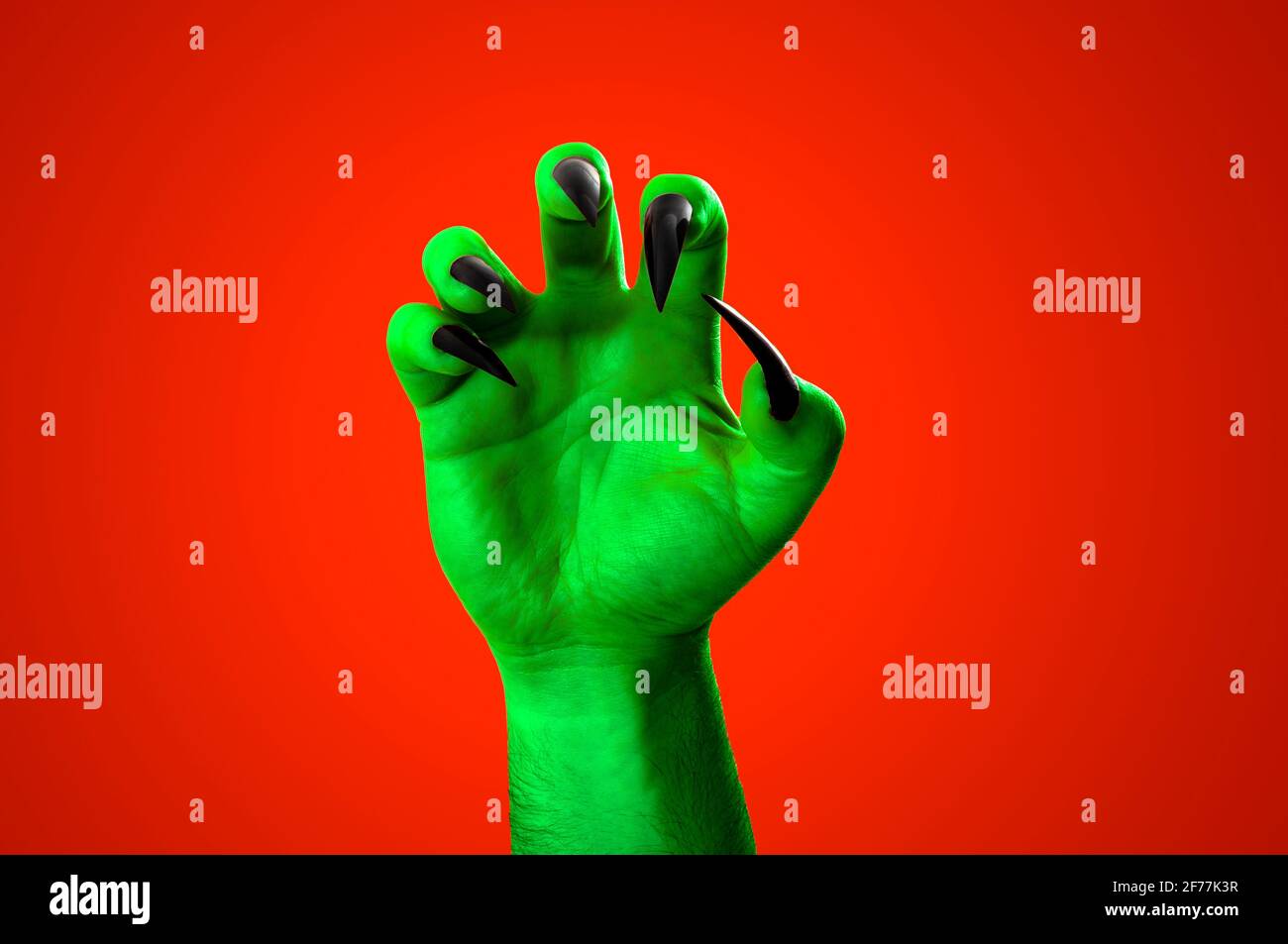Halloween, nightmare creature and evil monster horror story concept with a scary zombie or demon hand with creepy long black nails isolated on orange Stock Photo