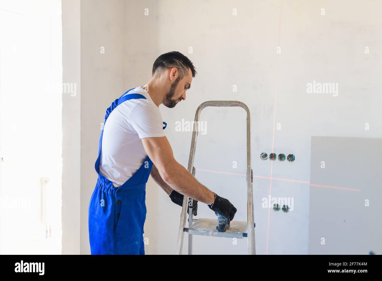 A man in overalls marks the wall using a laser level Stock Photo