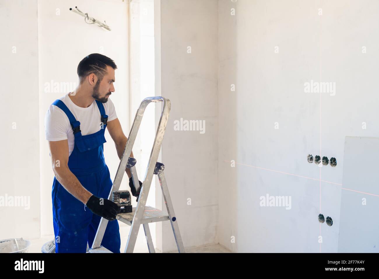 A adjuster in overalls marks the wall using a laser level Stock Photo