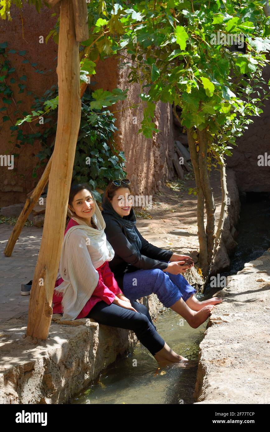 Iran, Isfahan province, Abyaneh, Young women enjoying the cool stream of an irrigation channel Stock Photo