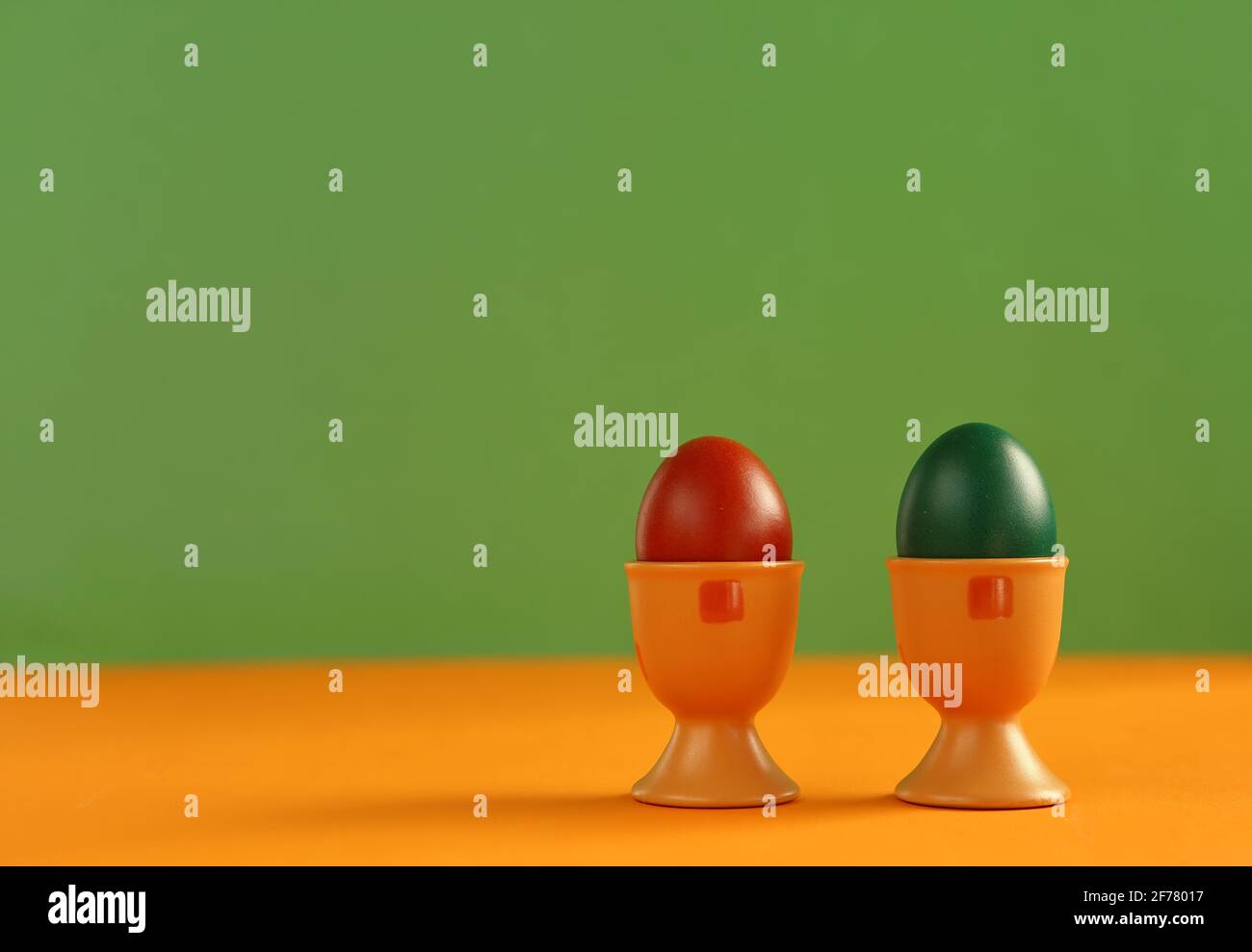 Two painted colorful easter eggs into eggcups close up on green and orange background Stock Photo