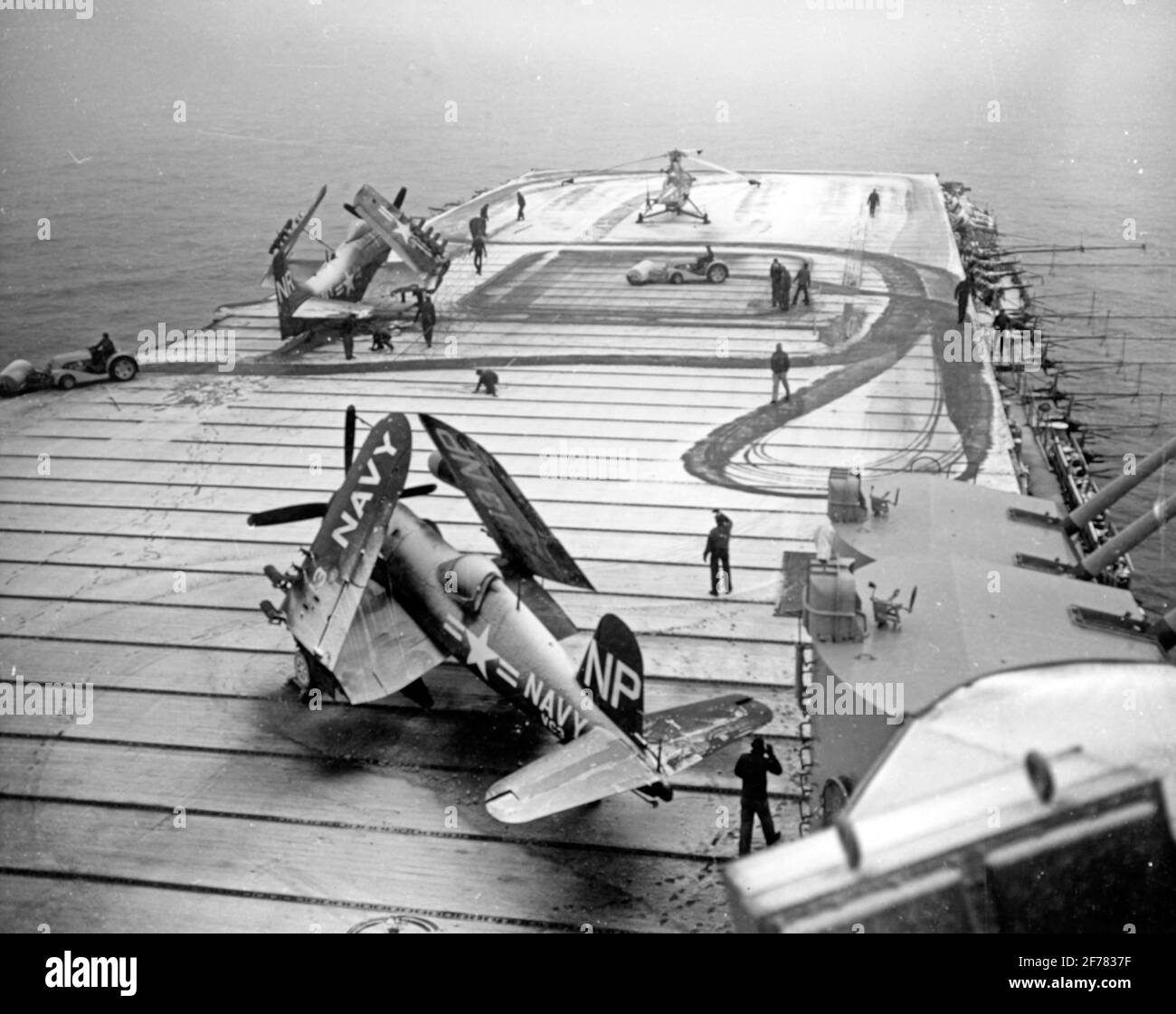 USS Valley Forge (CV-45) Crewmen use flight deck tractors with power brooms to sweep snow from the carrier's flight deck, during operations off Korea, circa early 1951. Photo is dated 8 May 1951, but Valley Forge ended her second Korean War deployment in late March of that year. Plane parked in the foreground is a F4U-4 Corsair fighter. Those on the forward flight deck are an AD Skyraider attack plane and a HO3S helicopter Stock Photo