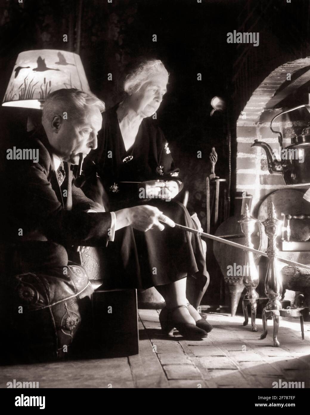 1930s MATURE SENIOR RETIRED COUPLE MAN AND WOMAN SITTING LOOKING INTO BRICK COLONIAL FIREPLACE MAN STOKING FIRE WITH POKER - f921 HAR001 HARS OLD FASHION RETIRED 1 SECURITY MYSTERY STRONG JOY LIFESTYLE SATISFACTION BRICK ELDER FEMALES MARRIED PIPE RURAL HEAT SPOUSE HUSBANDS HOME LIFE COPY SPACE FRIENDSHIP HALF-LENGTH LADIES PERSONS INSPIRATION CARING MALES WARM RETIREMENT SENIOR MAN SENIOR ADULT B&W PARTNER SENIOR WOMAN COMFORT POKER RETIREE HAPPINESS OLD AGE OLDSTERS OLDSTER LEISURE PIPES TOBACCO DRAMATIC LAMPSHADE BAD HABIT SMOKER ELDERS NICOTINE CONNECTION CONCEPTUAL WARMTH ADDICTIVE COZY Stock Photo