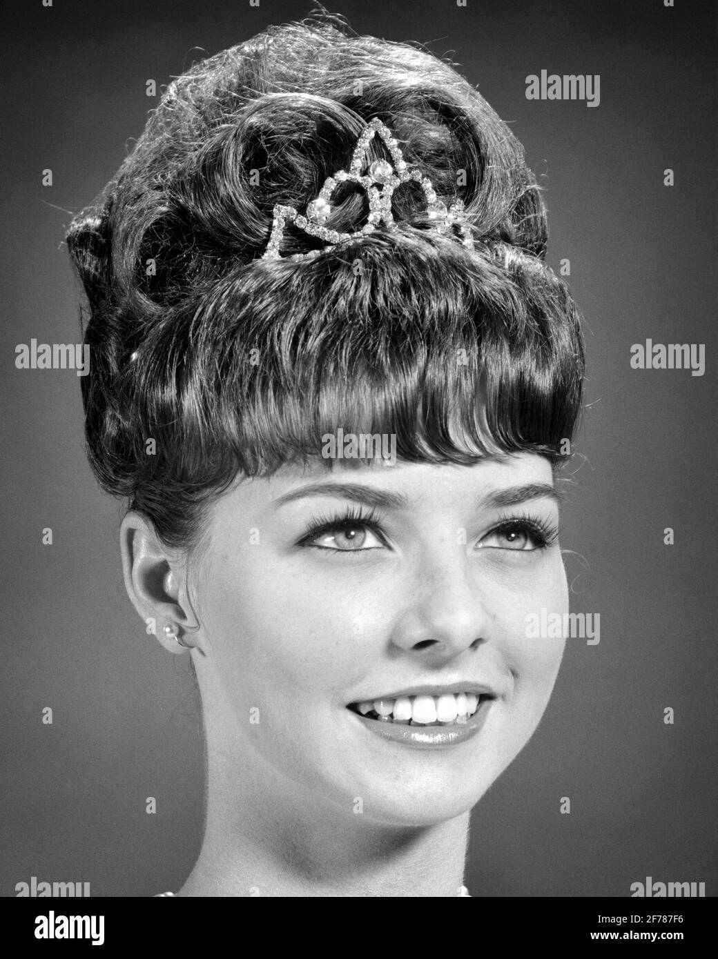 1960s SMILING YOUNG WOMAN WITH BRUNETTE BEEHIVE HAIRDO WEARING RHINESTONE TIARA  - f11745 HAR001 HARS HAIRSTYLE OCCASION TEASED HAIR PRIDE RHINESTONE BY STYLISH TEENAGED JEWELED HAIRDO WORN BANGS BIG HAIR BLACK AND WHITE BOUFFANT CAUCASIAN ETHNICITY DURING HAR001 OLD FASHIONED PRINCESS Stock Photo