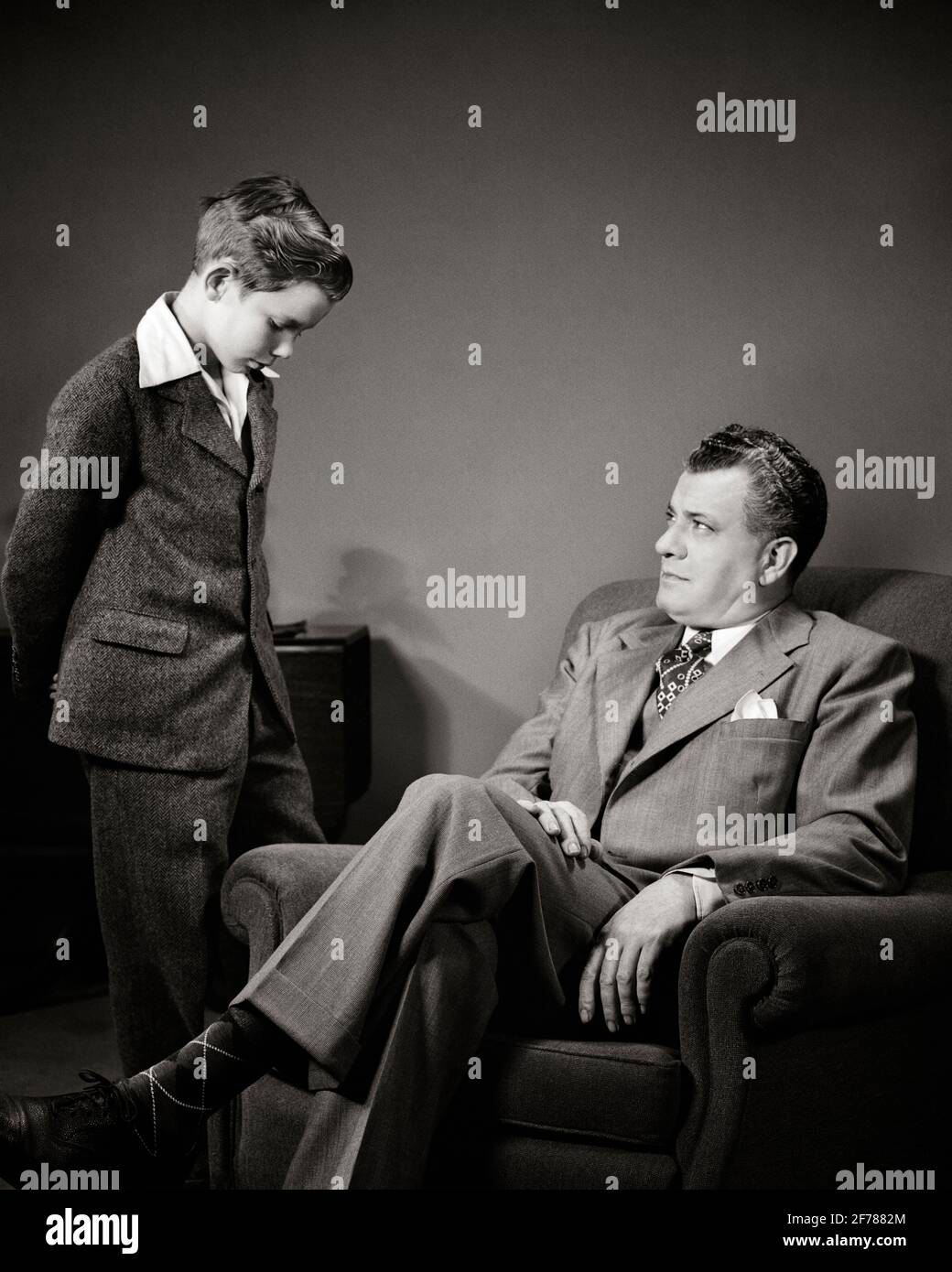 1940s MAN FATHER SEATED TALKING TO DISCIPLINING ADMONISHING PRE-TEEN BOY SON STANDING WITH HEAD BOWED ASHAMED - j4426 HAR001 HARS FACIAL ANGER COMMUNICATION STRONG SONS CONTROL FAMILIES LIFESTYLE PARENTING STUDIO SHOT HOME LIFE SEATED COPY SPACE FRIENDSHIP HALF-LENGTH PERSONS DISCIPLINE CARING MALES TEENAGE BOY EXPRESSIONS FATHERS B&W LECTURE HIGH ANGLE HIS SORRY DADS AUTHORITY DISCIPLINED RULES ASHAMED CONCEPTUAL TEENAGED OBEY PERSONAL ATTACHMENT AFFECTION BEHAVIOR BOWED EMOTION JUVENILES MID-ADULT MID-ADULT MAN OBEDIENCE PARENTAL PRE-TEEN PRE-TEEN BOY SCOLD TOGETHERNESS BLACK AND WHITE Stock Photo
