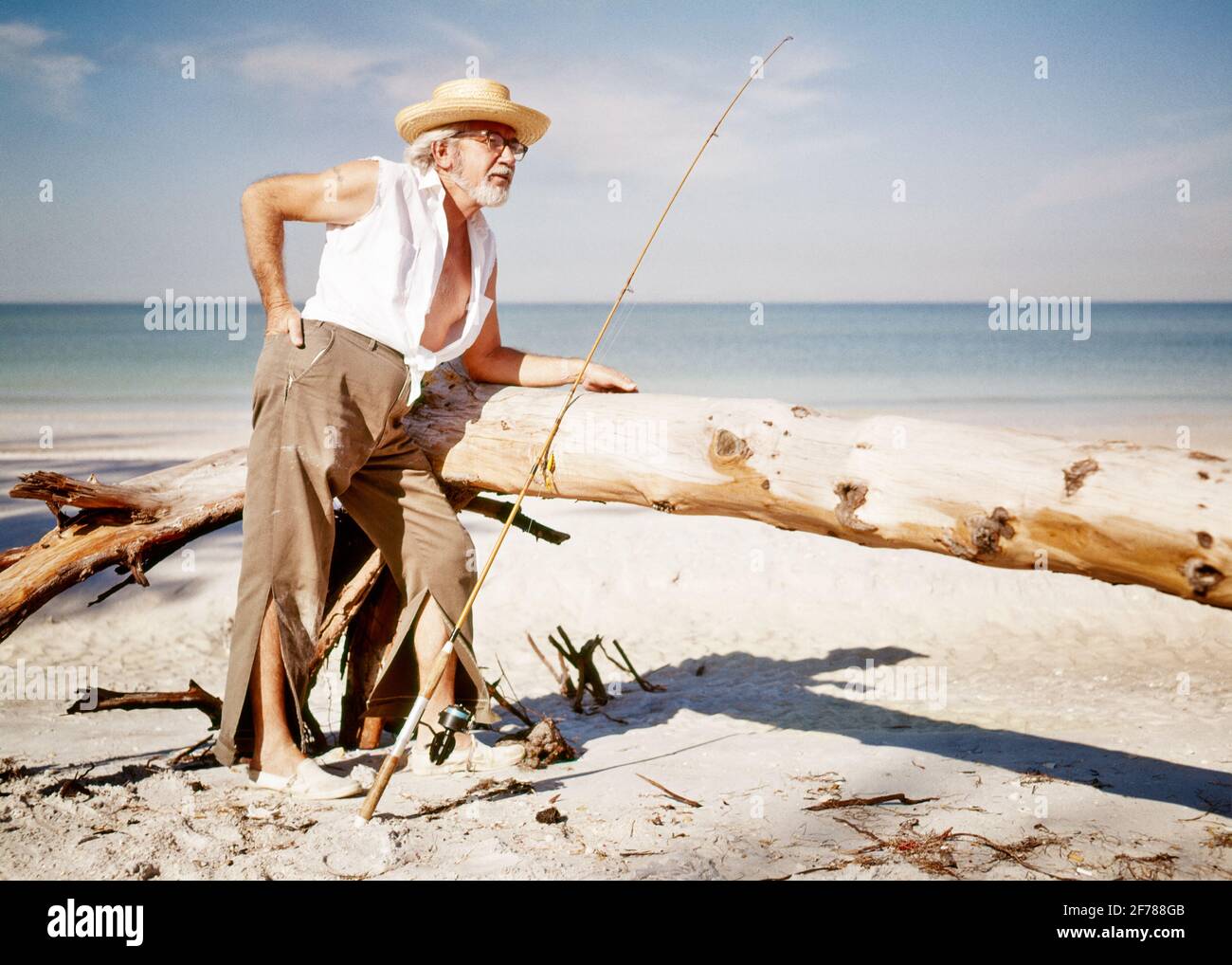 1970S RETIRED SENIOR MAN RAGGED CLOTHES FISHING ON TROPICAL