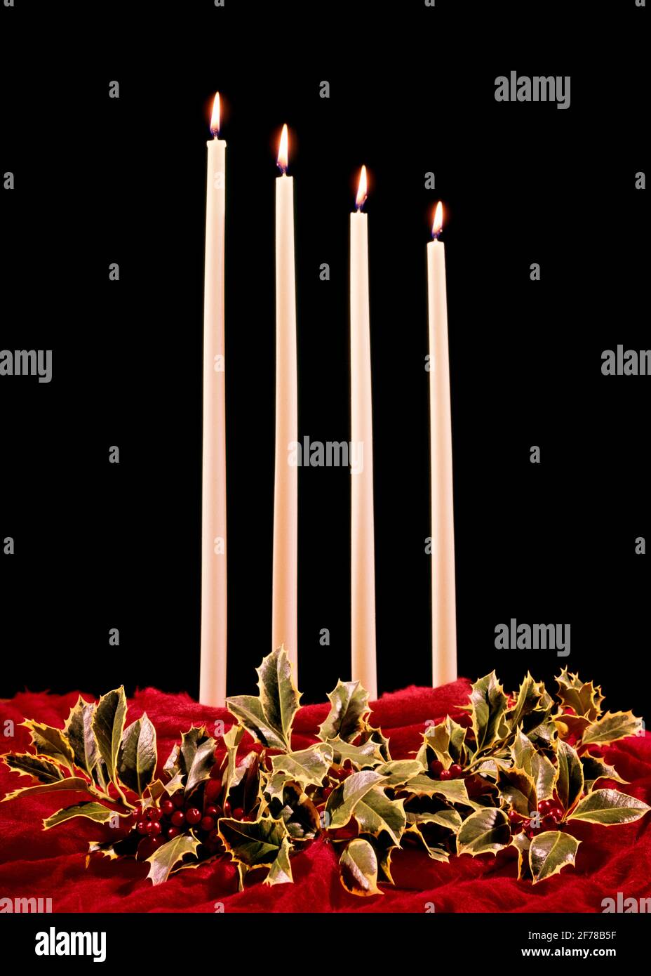 1960s CHRISTMAS STILL LIFE DECORATION FOUR BURNING TALL WHITE WAX CANDLES AND SURROUNDING HOLLY LEAVES AND BERRIES ON RED FABRIC - kx3750 HAR001 HARS SYMBOLIC BERRIES CONCEPTS JOYOUS FESTIVE HAR001 LIGHTED OLD FASHIONED REPRESENTATION Stock Photo