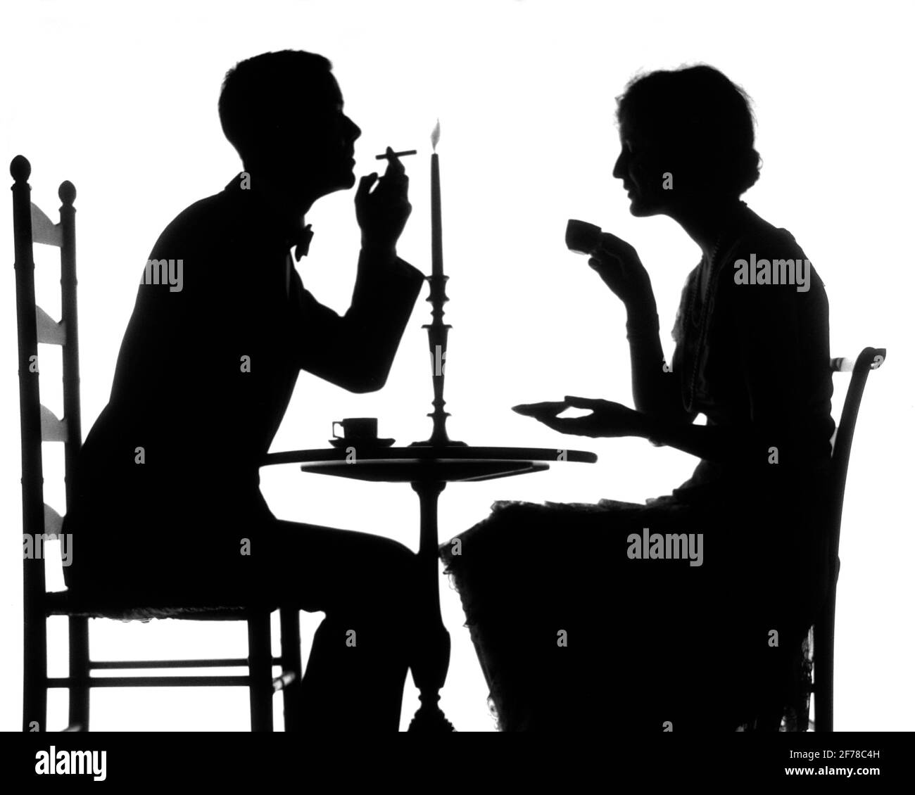 1920s SILHOUETTE OF COUPLE SITTING AT TABLE WOMAN DRINKING CUP OF TEA COFFEE MAN LIGHTING CIGARETTE FROM CANDLE FLAME - s1309 HAR001 HARS MYSTERY STRONG FLAME LIFESTYLE LIGHTING FEMALES MARRIED STUDIO SHOT SPOUSE HUSBANDS HOME LIFE COPY SPACE FRIENDSHIP FULL-LENGTH LADIES PERSONS CARING MALES SILHOUETTES B&W OUTLINE PARTNER DATING CIGARETTES HAPPINESS BEVERAGE TOBACCO SILHOUETTED FLUID ATTRACTION BAD HABIT SMOKER NICOTINE COURTSHIP CONCEPTUAL ADDICTIVE STYLISH ANONYMOUS CAFFEINE JOE PERSONAL ATTACHMENT POSSIBILITY AFFECTION EMOTION JAVA MID-ADULT MID-ADULT MAN MID-ADULT WOMAN SOCIAL ACTIVITY Stock Photo