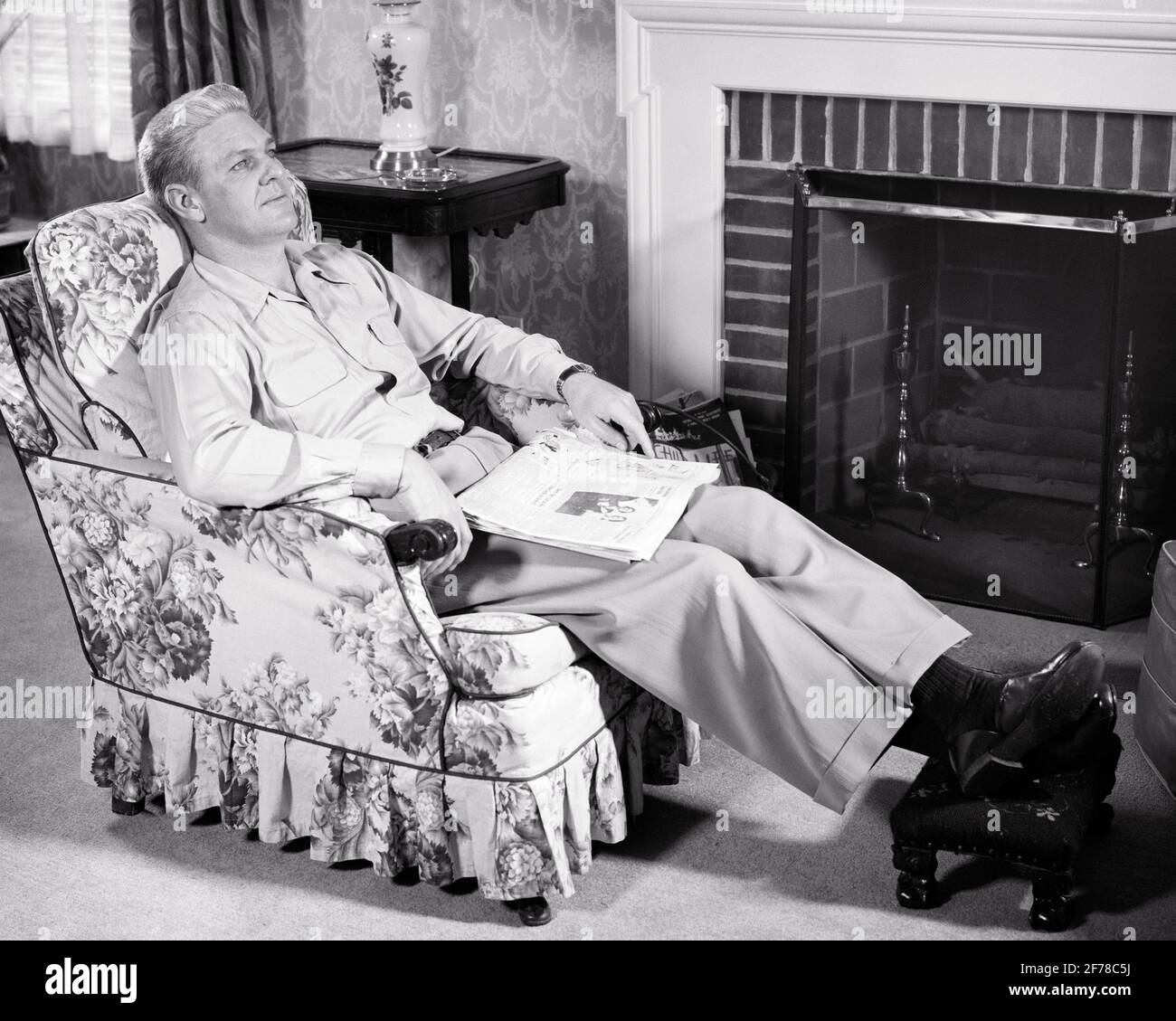 1950s MAN RESTING THINKING SITTING IN CHINTZ COVERED EASY CHAIR IN LIVING ROOM WITH NEWSPAPER FOLDED IN HIS LAP - s1073 HAR001 HARS REFLECTIVE THINK EASY CHAIR IN REFLECTING PONDER PONDERING CONSIDER LOST IN THOUGHT EASY FOOTSTOOL UPHOLSTERY CHINTZ CONTEMPLATIVE MEDITATE MEDITATIVE MID-ADULT MID-ADULT MAN RELAXATION REST BLACK AND WHITE CAUCASIAN ETHNICITY CONSIDERING HAR001 OLD FASHIONED Stock Photo