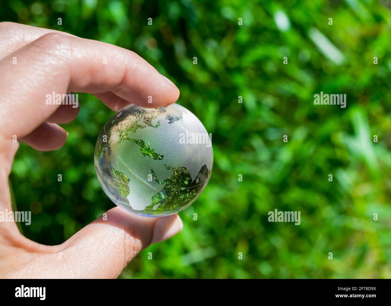 Crystal globe in the hand of a man against a background of green foliage. Earth protection concept. Earth Day Stock Photo