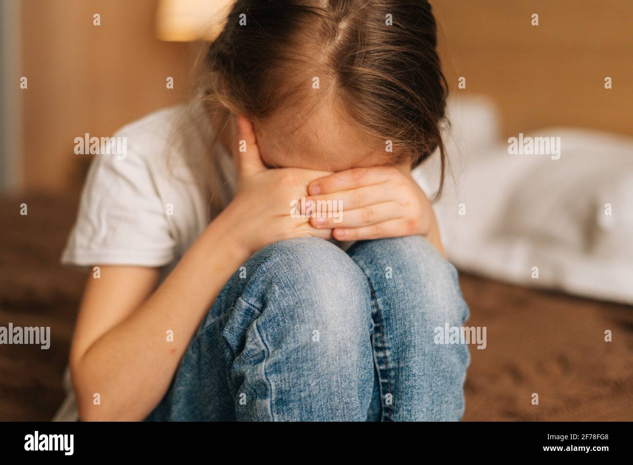 Closeup of disappointed little girl hugging knee, sobbing with head bowed and crying sitting