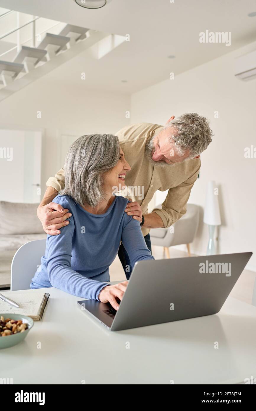 Happy mature senior couple laughing using laptop computer at home. Stock Photo