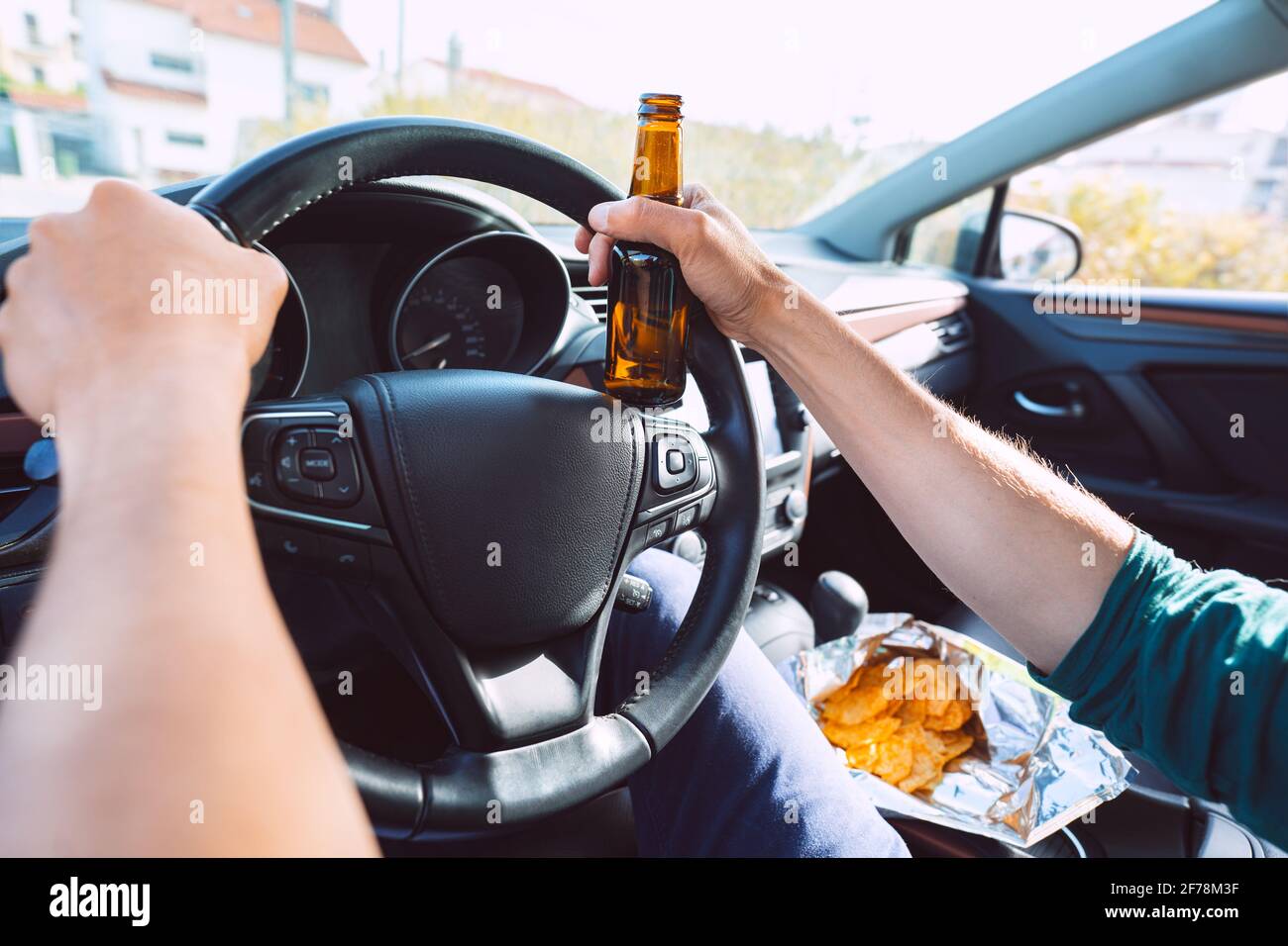 Young drunk man drives a car with a bottle of beer. Driving under alcohol influence. Drunk driving Stock Photo