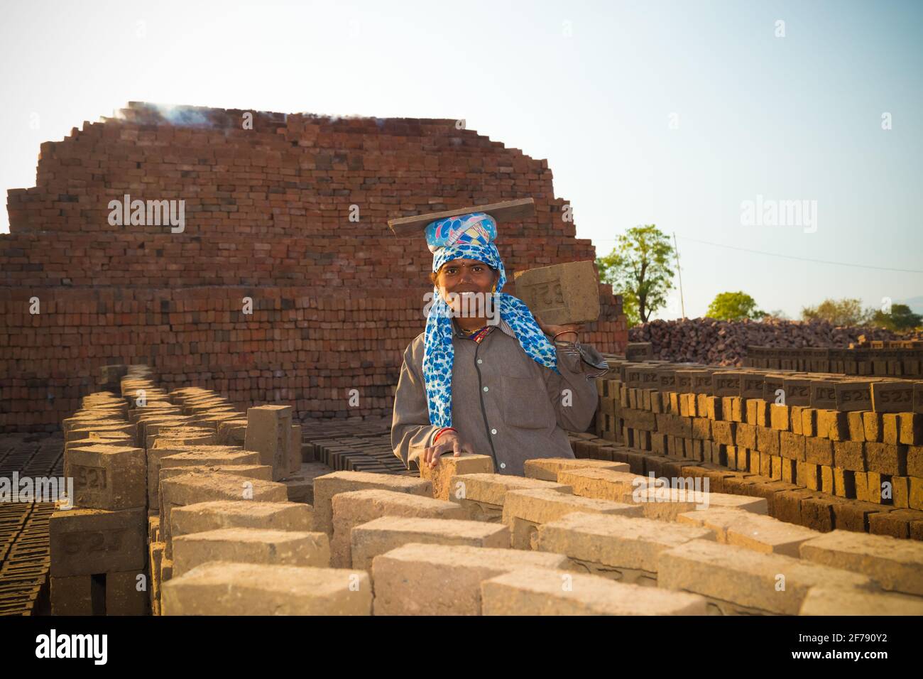 An independent, beautiful, hard working woman, working in the brick kiln site. Active traditional brick kiln in the backdrop. Stock Photo