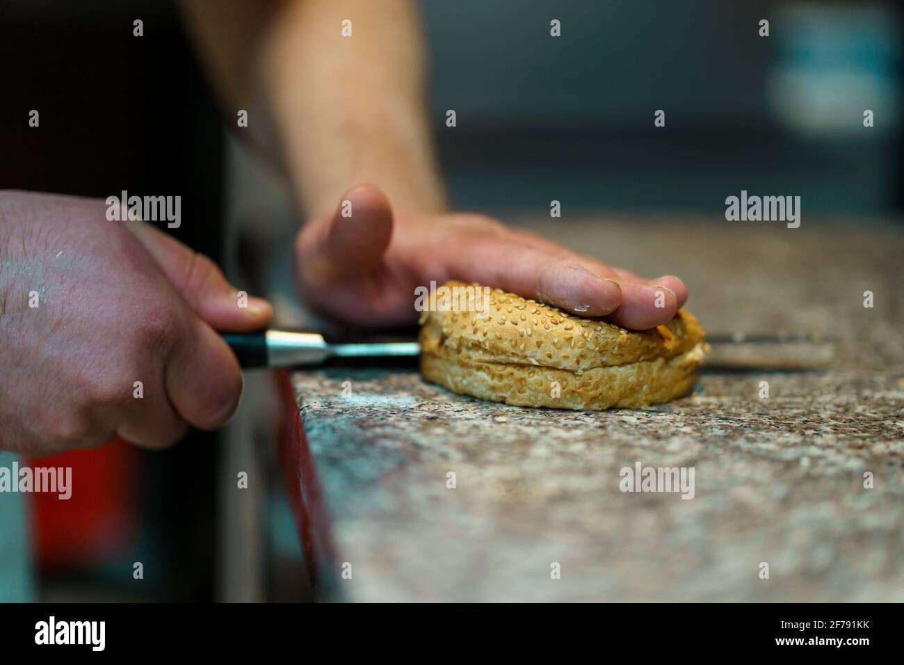Close up on hands of unknown caucasian man chef cutting bun on the counter-top in the kitchen at restaurant Stock Photo