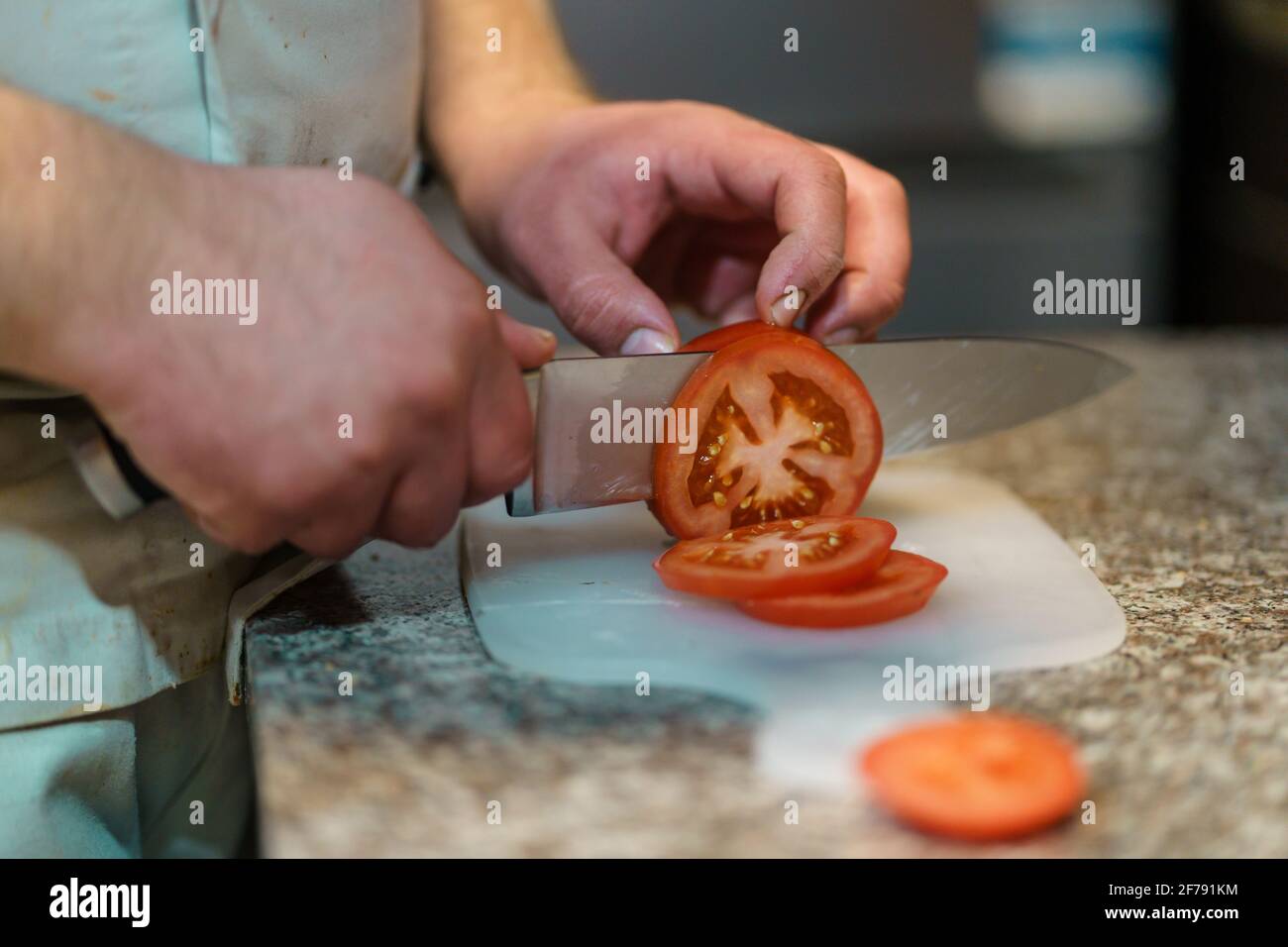 Close up on hands of unknown caucasian man chef cutting tomato on the counter-top in the kitchen at restaurant Stock Photo